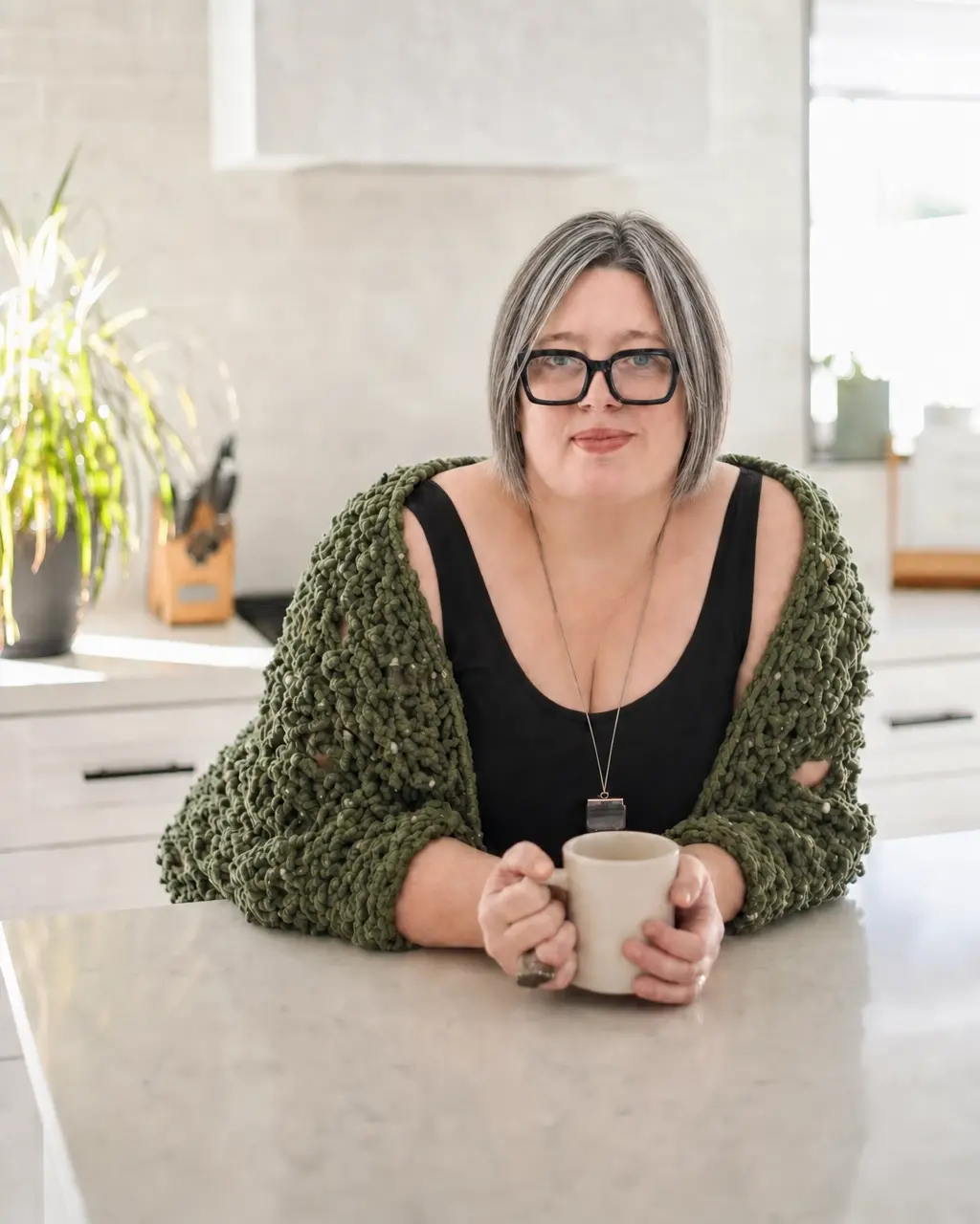 Amy, the founder + cook, leaning on her kitchen island holding a mug in a bright, airy home kitchen